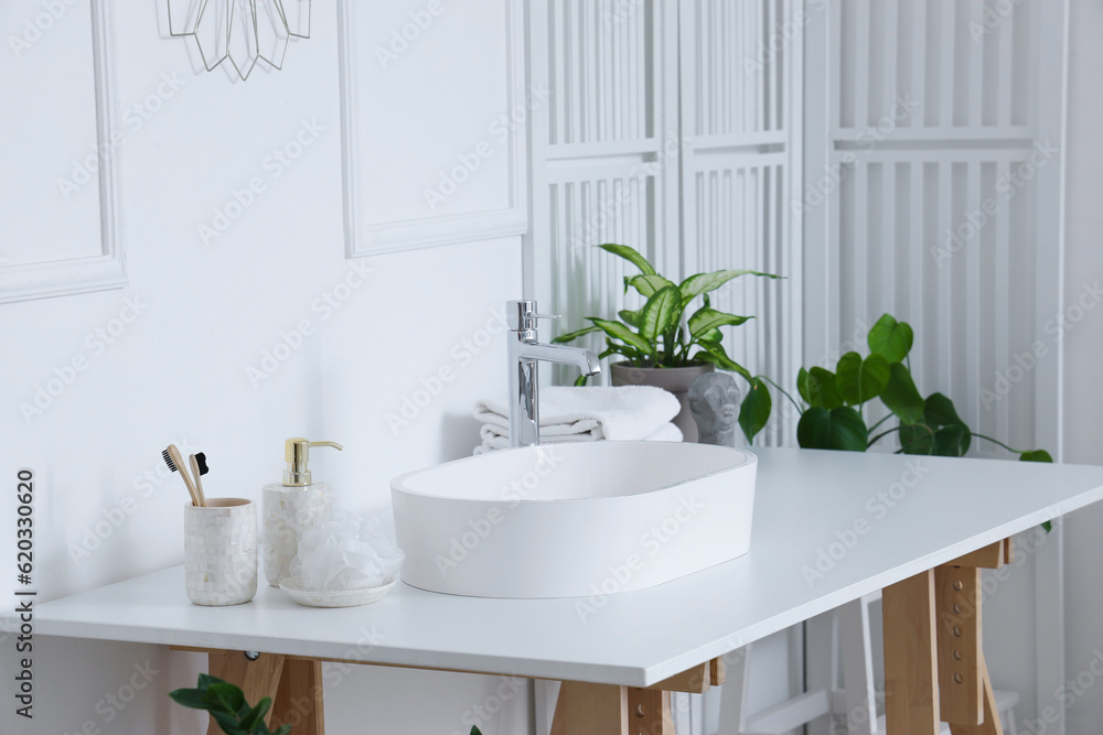 Fototapeta premium Interior of light bathroom with white sink, bath accessories and houseplants