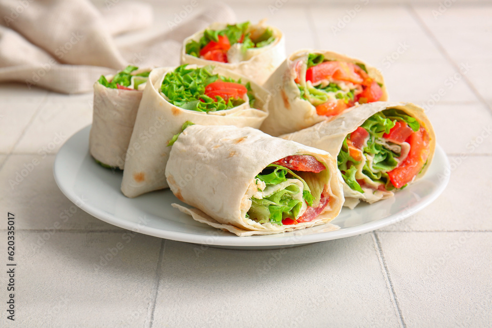 Plate of tasty lavash rolls with tomatoes and greens on white tile background