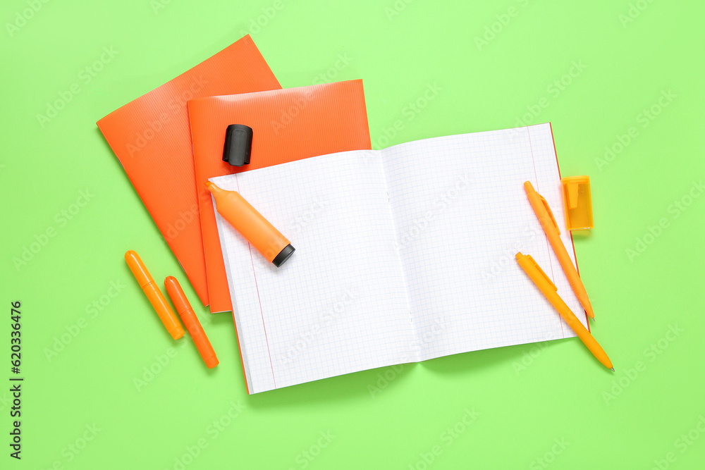 Orange notebooks with markers on green background Orange notebooks with markers on green background