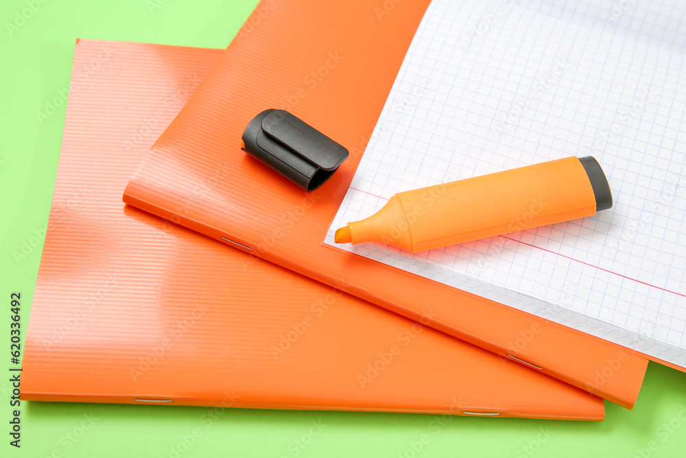 Orange notebooks with markers on green background Orange notebooks with markers on green background