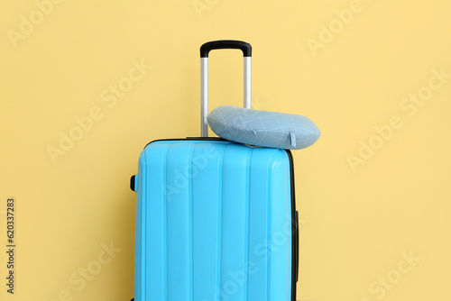 Blue suitcase with travel cushion near yellow wall. Travel concept
