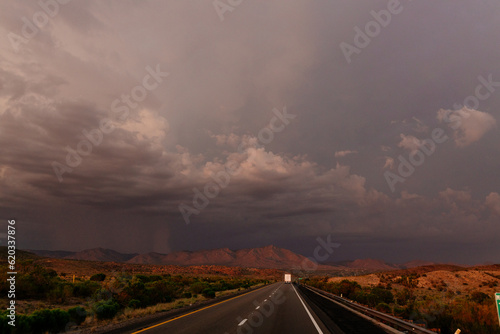 A beautiful asphalt road among hills with dry grass. A scenic landscape with highway, mountains on background and blue sky with fluffy clouds on sunny day. Phoenix, AZ, USA - 7-22-2021