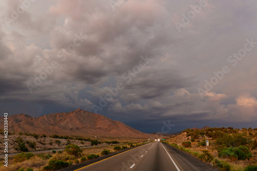 A beautiful asphalt road among hills with dry grass. A scenic landscape with highway, mountains on background and blue sky with fluffy clouds on sunny day. Phoenix, AZ, USA - 7-22-2021