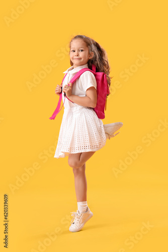 Jumping little schoolgirl on yellow background