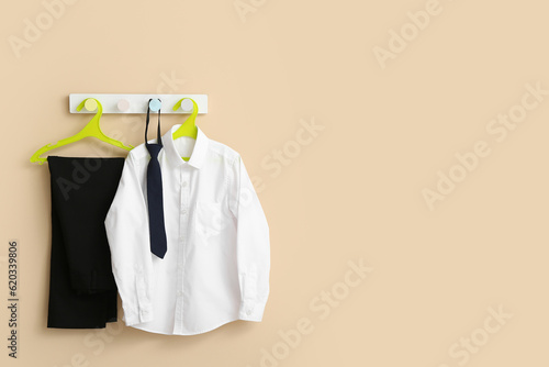 Stylish school uniform hanging on rack against beige wall