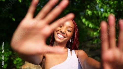 Outdoor portrait natural Beautiful young African American woman red braids hair style, perfect white teeth smile, laughing closing camera with hands at sunny summer day with green foliage background