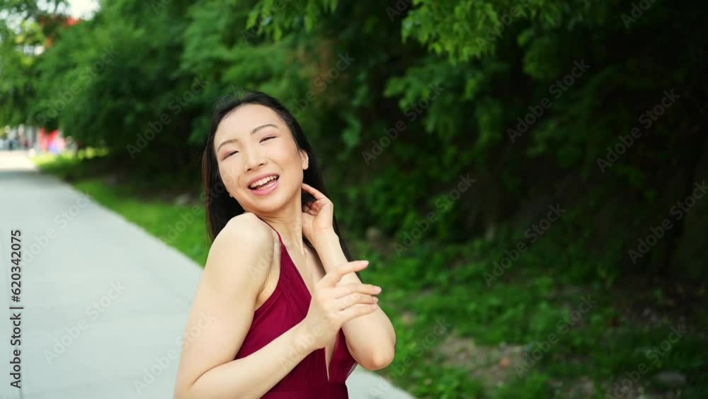 Street style outdoor portrait of Beautiful young Chinese Asian happy smiling woman walking outside sunny summer day. Attractive woman enjoys posing in front of parked cars. Big city life concept Street style outdoor portrait of Beautiful young Chinese Asian happy smiling woman walking outside sunny summer day. Attractive woman enjoys posing in front of parked cars. Big city life concept