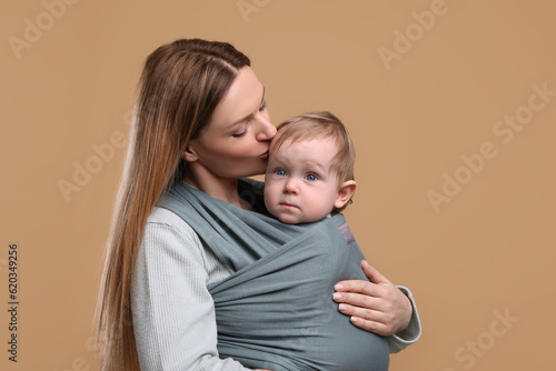 Mother holding her child in baby wrap on light brown background
