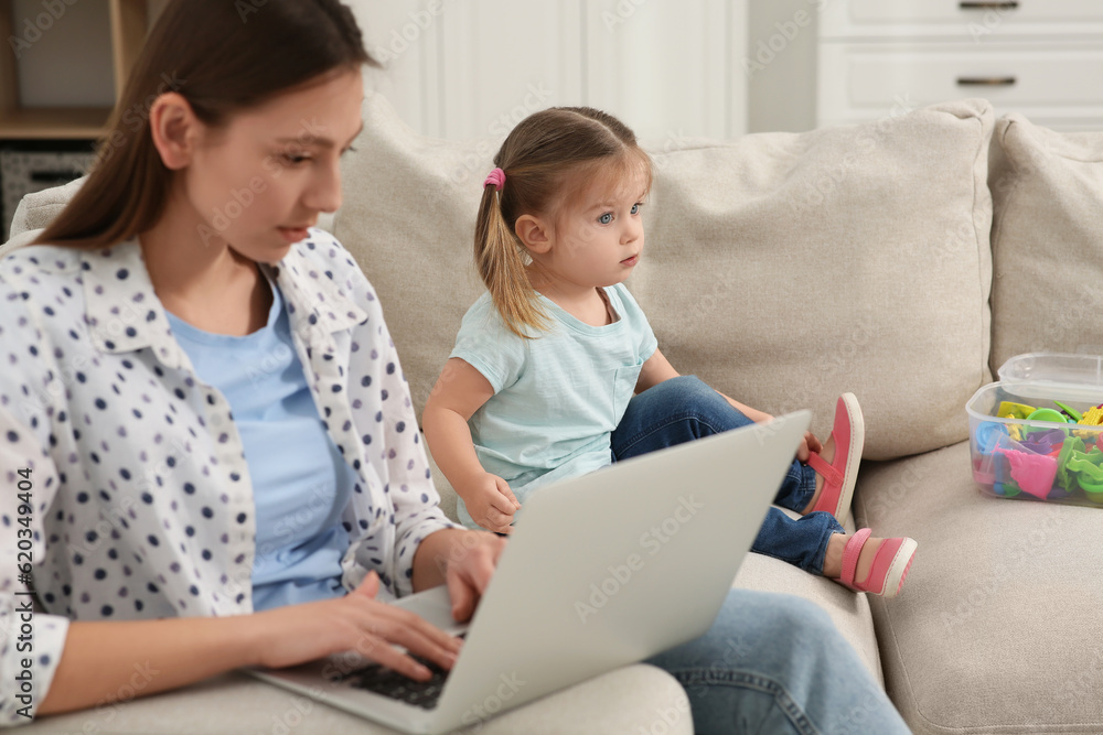 Woman with laptop working remotely at home. Mother and daughter on sofa in living room Woman with laptop working remotely at home. Mother and daughter on sofa in living room
