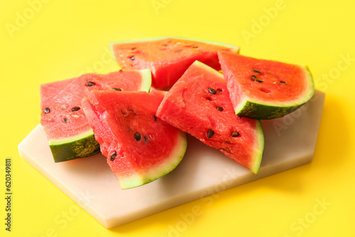 Board with pieces of fresh watermelon on yellow background