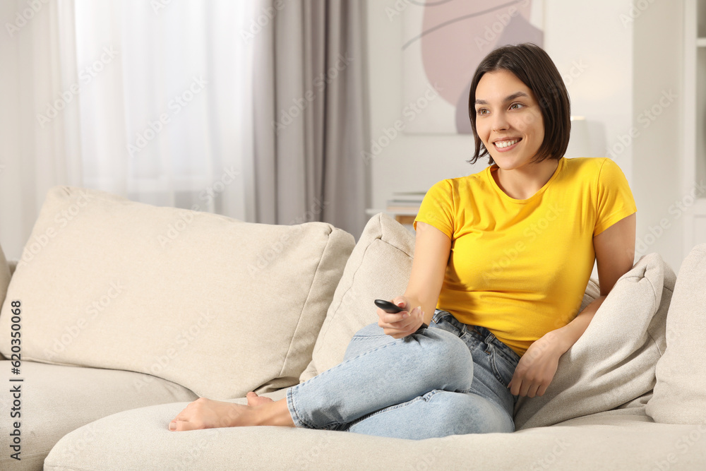 Happy woman watching TV on sofa indoors, space for text Happy woman watching TV on sofa indoors, space for text