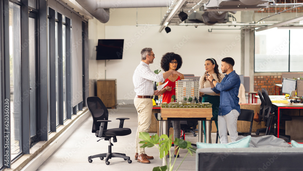 Diverse business people looking at architectural model and discussing work at office Diverse business people looking at architectural model and discussing work at office