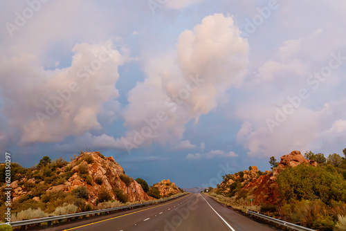 A beautiful asphalt road among hills with dry grass. A scenic landscape with highway, mountains on background and sunset sky. Phoenix, AZ, USA - 7-22-2021