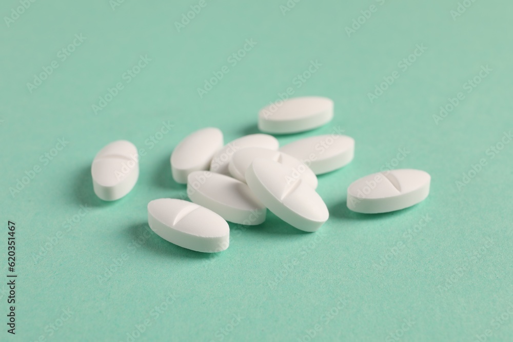 Pile of white pills on green background, closeup
