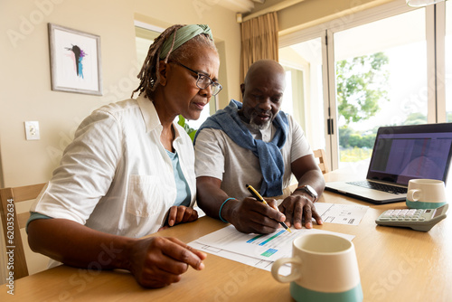 Senior african american couple sitting at table using laptop and paying bills at home photo