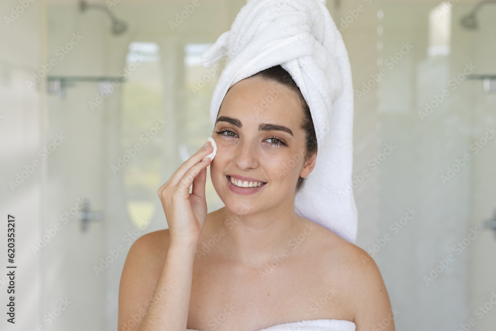 Portrait of happy caucasian woman with towel on head using pad on face in bathroom Portrait of happy caucasian woman with towel on head using pad on face in bathroom