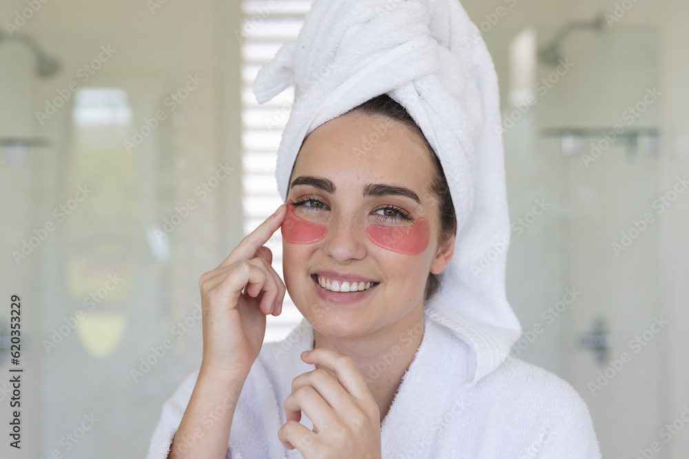 Portrait of happy caucasian woman with towel on head applying eye patches in bathroom Portrait of happy caucasian woman with towel on head applying eye patches in bathroom