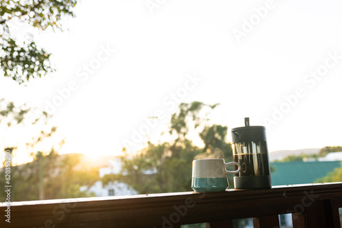 Coffee press and mug of fresh coffee at balcony on sunny day