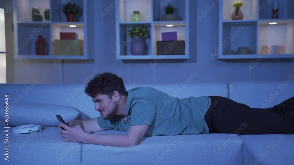 Man lying on the sofa at night texting on the phone. Happy and in good spirits. Man lying on the sofa at night texting on the phone. Happy and in good spirits.