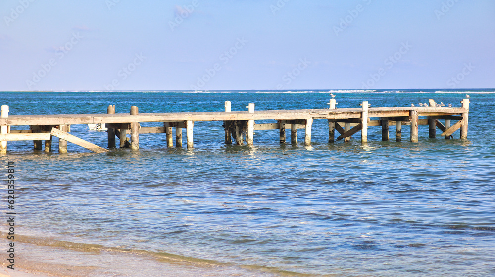 beach boardwalk made of wood in the stretches into the Caribbean sea ocean turquoise blue water with blue sky in the background