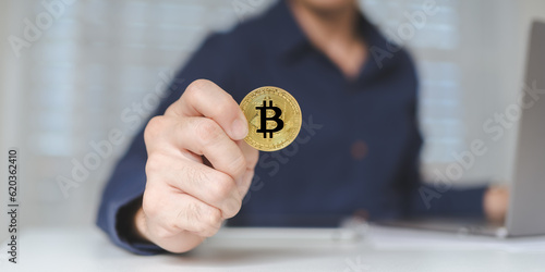 Bitcoin Cryptocurrency investment concept. Trader or investor hand holds Bitcoin Cryptocurrency gold coins. Businessman shows Bitcoin Cryptocurrency on hands while using laptop for trading. Banner.