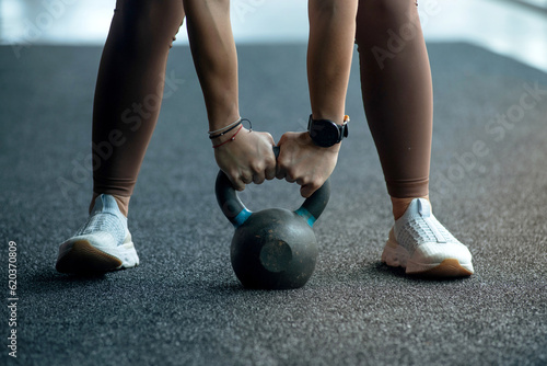 Woman preparing for workout with kettlebell weight at indoor fitness gym, lower body legs and feet closeup of strength training legs