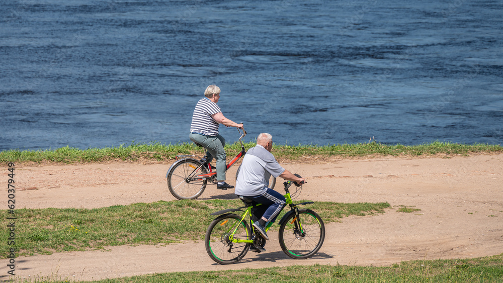 Senior couple rides bicycles along a rural road along the river bank. Senior couple rides bicycles along a rural road along the river bank.