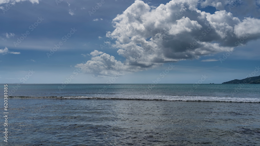 The wave foams in the boundless turquoise ocean. Picturesque cumulus clouds in a blue sky. Seychelles.