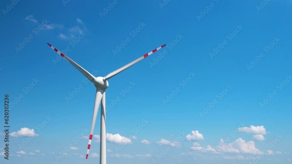 A spinning wind turbine against a sky-blue sky with small clouds. The main part of the wind turbine is on the left side. Slow motion. A spinning wind turbine against a sky-blue sky with small clouds. The main part of the wind turbine is on the left side. Slow motion.