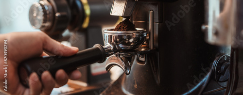 Coffee grinder grinds fresh coffee beans into a portafilter for  espresso machine. Barista grind coffee bean with grinder machine. Selective focus. photo
