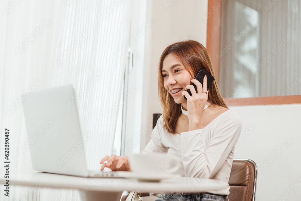 Asian woman working on computer laptop and using smartphone talking to customer or colleague. Businesswoman working online with computer laptop at coffee shop. Asian woman working on computer laptop and using smartphone talking to customer or colleague. Businesswoman working online with computer laptop at coffee shop.