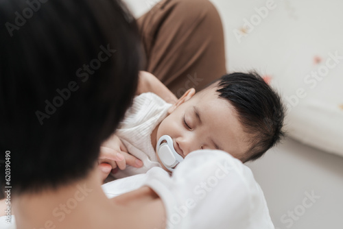 Top view, Young Asian mother holding her son baby sleeping on hand. Mom nurturing love newborn baby. Mom nursing baby. Happy asian family healthcare love together mother’s day concept.