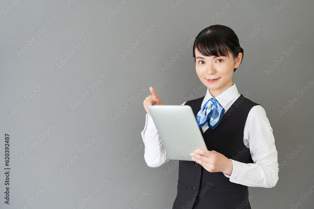 タブレットを操作するベストにリボンタイの制服を着た、受付業務、事務業務の女性 タブレットを操作するベストにリボンタイの制服を着た、受付業務、事務業務の女性