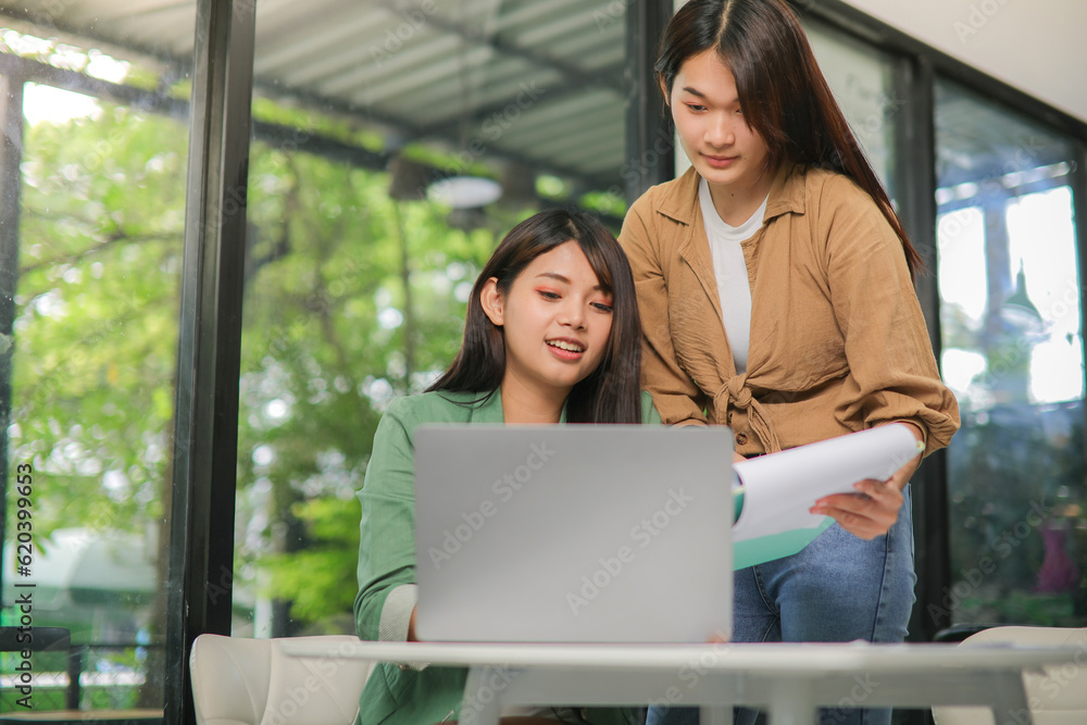 Two Asian women are consulting in the workplace. and see the work in the notebook Two Asian women are consulting in the workplace. and see the work in the notebook