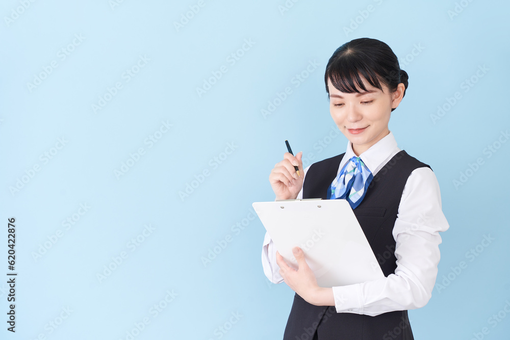 書類を書くベストにリボンタイの制服を着た、受付業務、事務業務の女性 書類を書くベストにリボンタイの制服を着た、受付業務、事務業務の女性