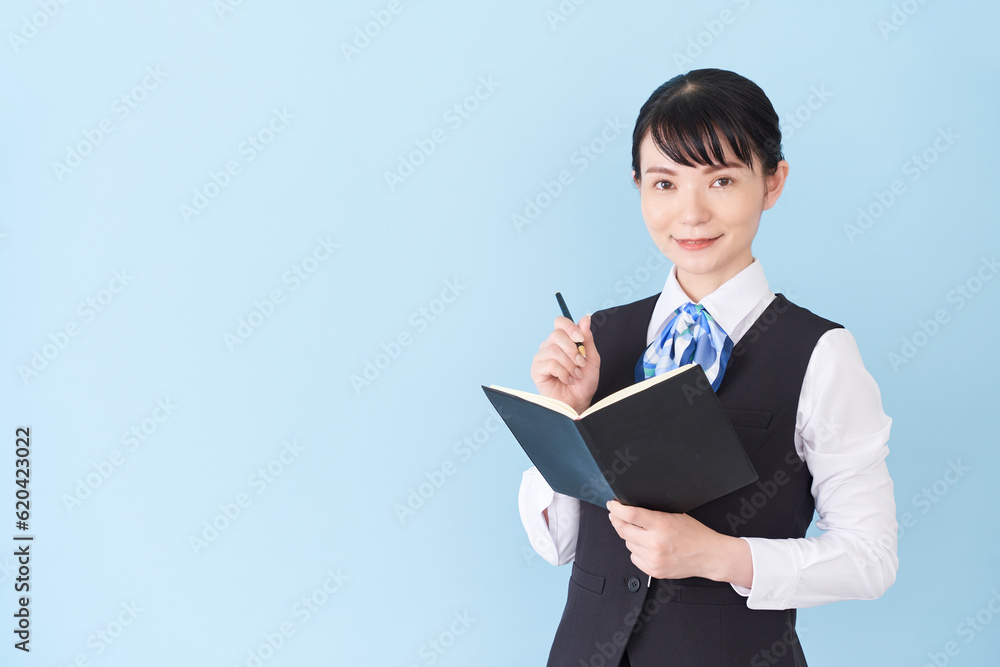 手帳を書くベストにリボンタイの制服を着た、受付業務、事務業務の女性 手帳を書くベストにリボンタイの制服を着た、受付業務、事務業務の女性