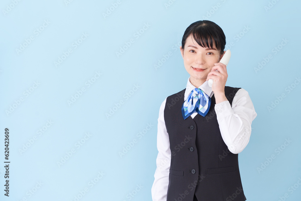 電話をするベストにリボンタイの制服を着た、受付業務、事務業務の女性
