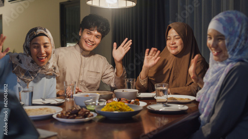Happy Asian muslim family celebrate long distance with cousin video call online Ramadan dinner together in dining room at home. Two generation celebration end of Eid al-Fitr togetherness at home.