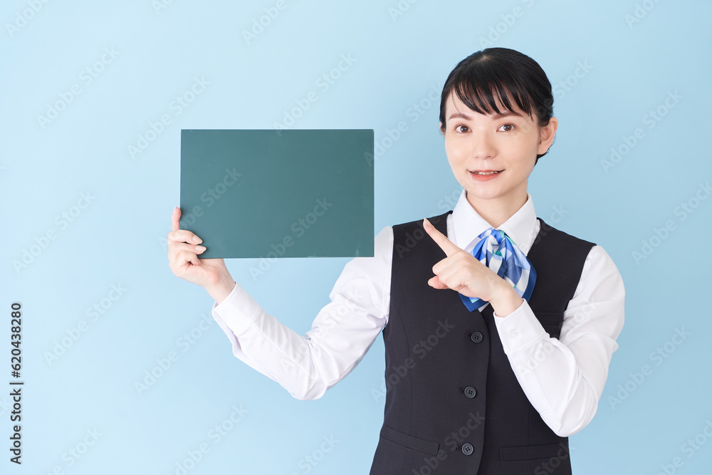 黒板を持つベストにリボンタイの制服を着た、受付業務、事務業務の女性