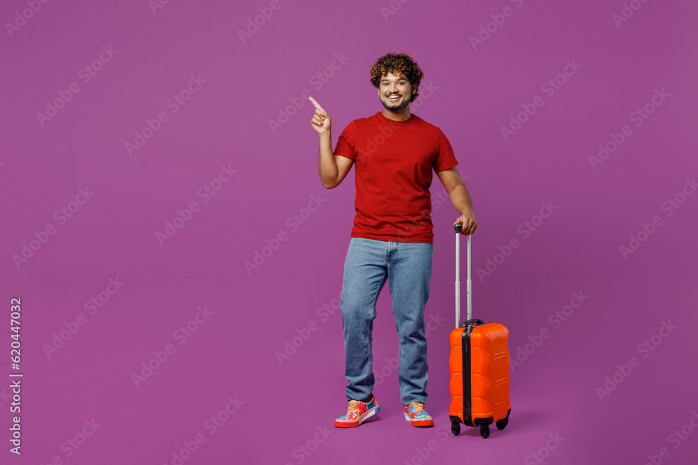 Traveler Indian man wears red t-shirt casual clothes hold bag point aside isolated on plain purple background. Tourist travel abroad in free spare time rest getaway. Air flight trip journey concept. Traveler Indian man wears red t-shirt casual clothes hold bag point aside isolated on plain purple background. Tourist travel abroad in free spare time rest getaway. Air flight trip journey concept.