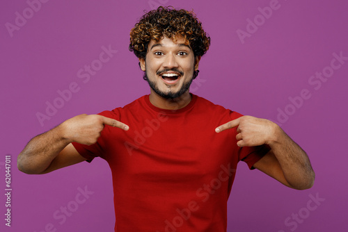 Young overjoyed surprised excited winner happy Indian man he wearing red t-shirt casual clothes point index fingers on himself isolated on plain purple background studio portrait. Lifestyle concept.