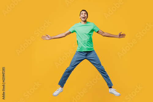 Full body excited young man of African American ethnicity he wear casual clothes green t-shirt hat jump high with outstretched hands legs isolated on plain yellow background studio. Lifestyle concept
