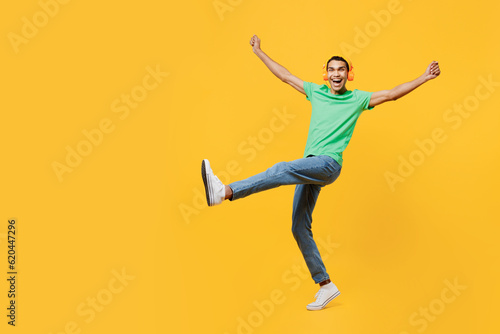 Full body happy young man of African American ethnicity he wears casual clothes green t-shirt hat listen to music in headphones isolated on plain yellow background studio portrait. Lifestyle concept. © ViDi Studio