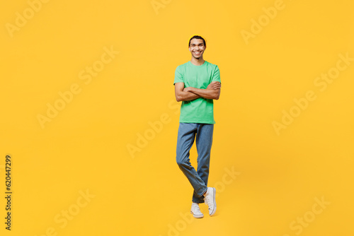 Full body young man of African American ethnicity he wears casual clothes green t-shirt hat hold hand crossed folded look camera isolated on plain yellow background studio portrait. Lifestyle concept