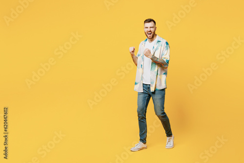 Full body side view young man wear blue shirt white t-shirt casual clothes doing winner gesture celebrate clenching fists say yes isolated on plain yellow background studio portrait Lifestyle concept