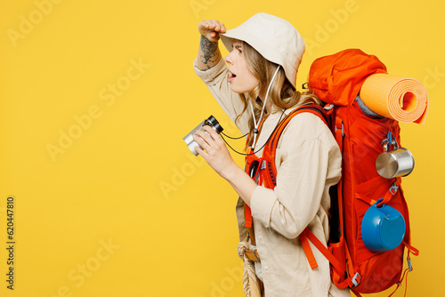 Young woman carry backpack with stuff mat use binocular look aside far away isolated on plain yellow background. Tourist leads active lifestyle walk on spare time Hiking trek rest travel trip concept. #620447810