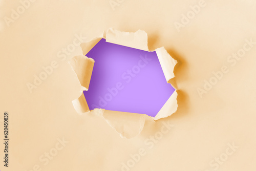 Torn hole in plain yellow paper with a purple background. Concept for advertising. 