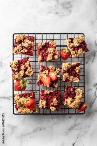 Strawberry granola bars on baking cooling rack white marble background . Delisious homemade oat squares for breakfast top view