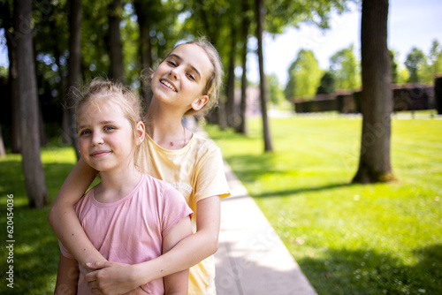 Two girls sisters of school age hug each other. A walk through the summer city park. Love and friendship within the family