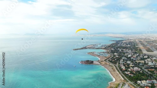 Drone follow Powered paraglider flyover turquoise water by Glyfada Coastline, Greece photo